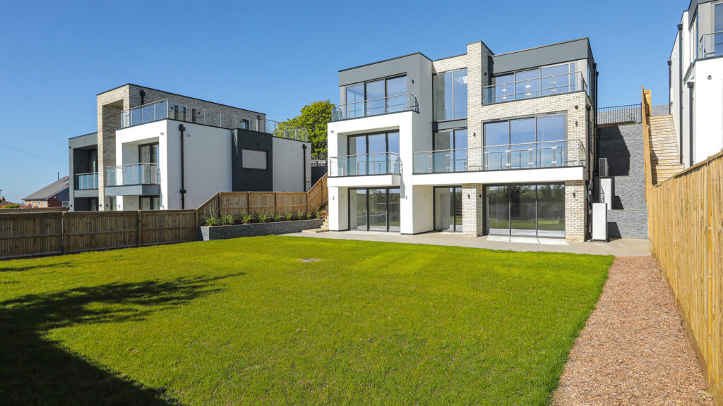 Rear view of modern multi-storey homes with large glass balconies, brick and white externals, and a spacious lawn garden.